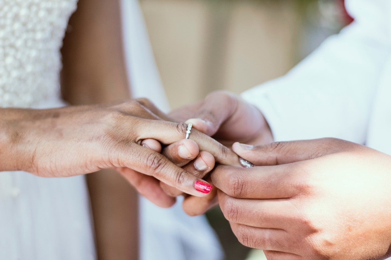 Close-up of a groom putting his bride’s diamond wedding band on her ring finger