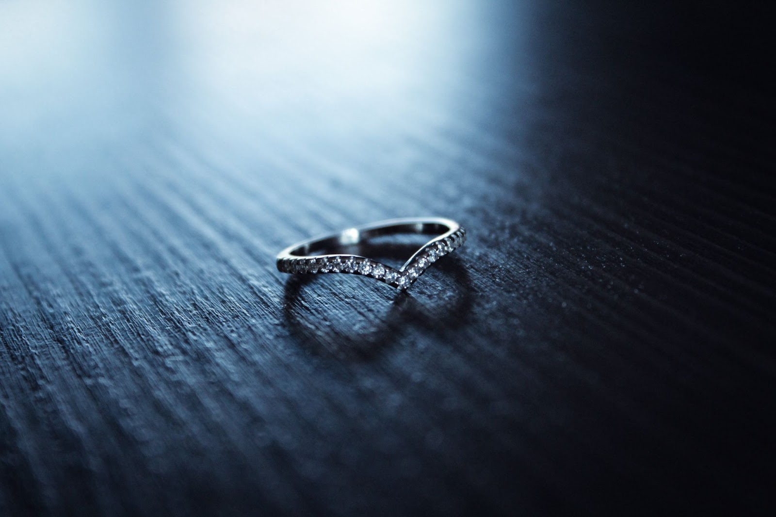 A curved, silver wedding band with diamond accents against a dark wood background