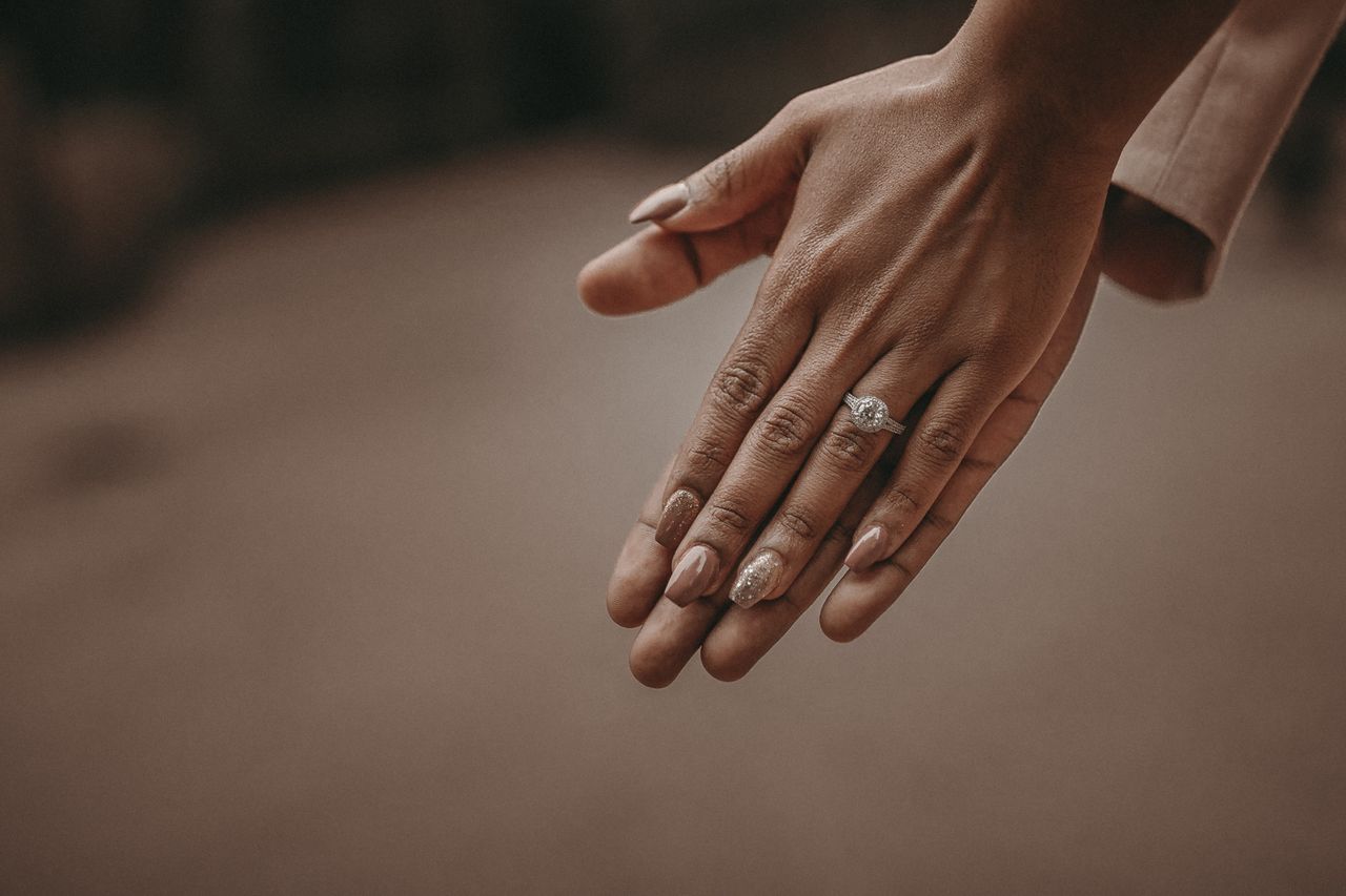 A woman wearing a round cut engagement ring rests her palm against her lover’s