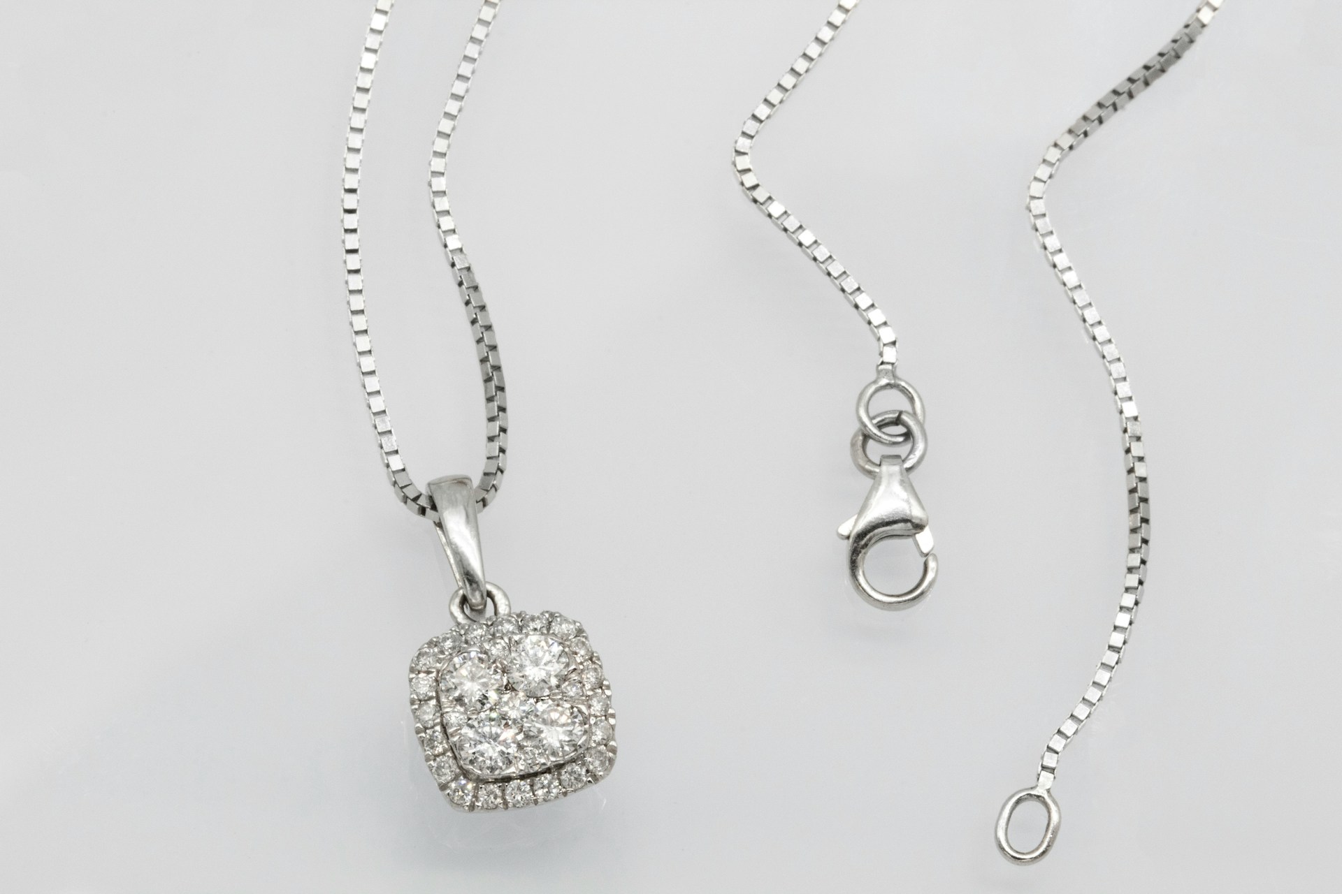 a white gold diamond pendant necklace on an off white surface