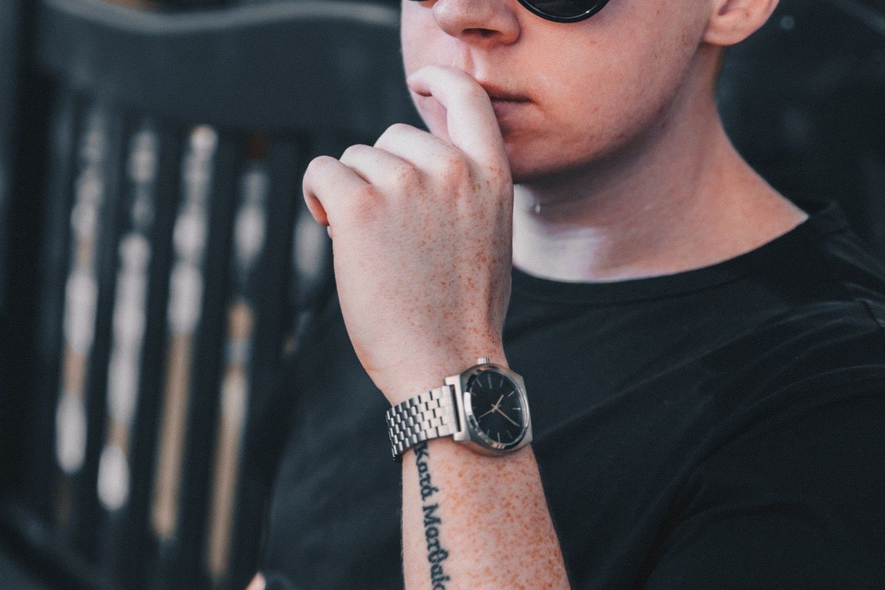 A man in a black short showcases his tattooed hand with a stainless steel wristwatch with black dial.