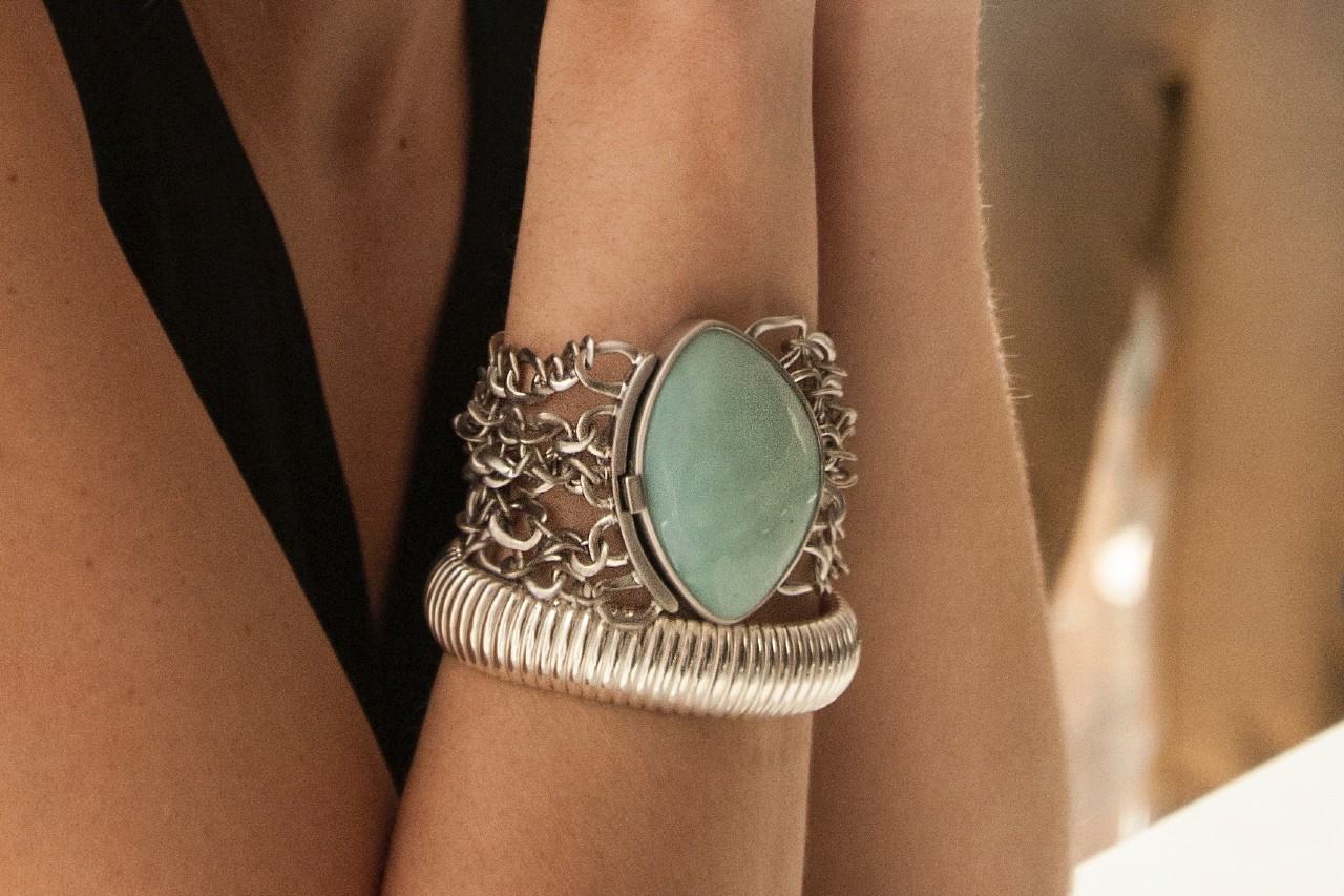 A close-up of a woman’s arm adorned with a big, chunky silver cuff with a large blue stone in the center, and another chunky silver bangle below it.