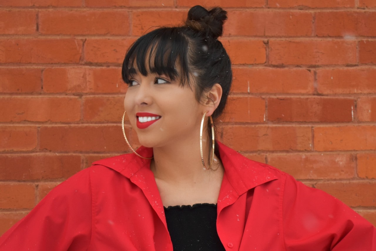A woman in a red top wearing large hoop earrings and smiling