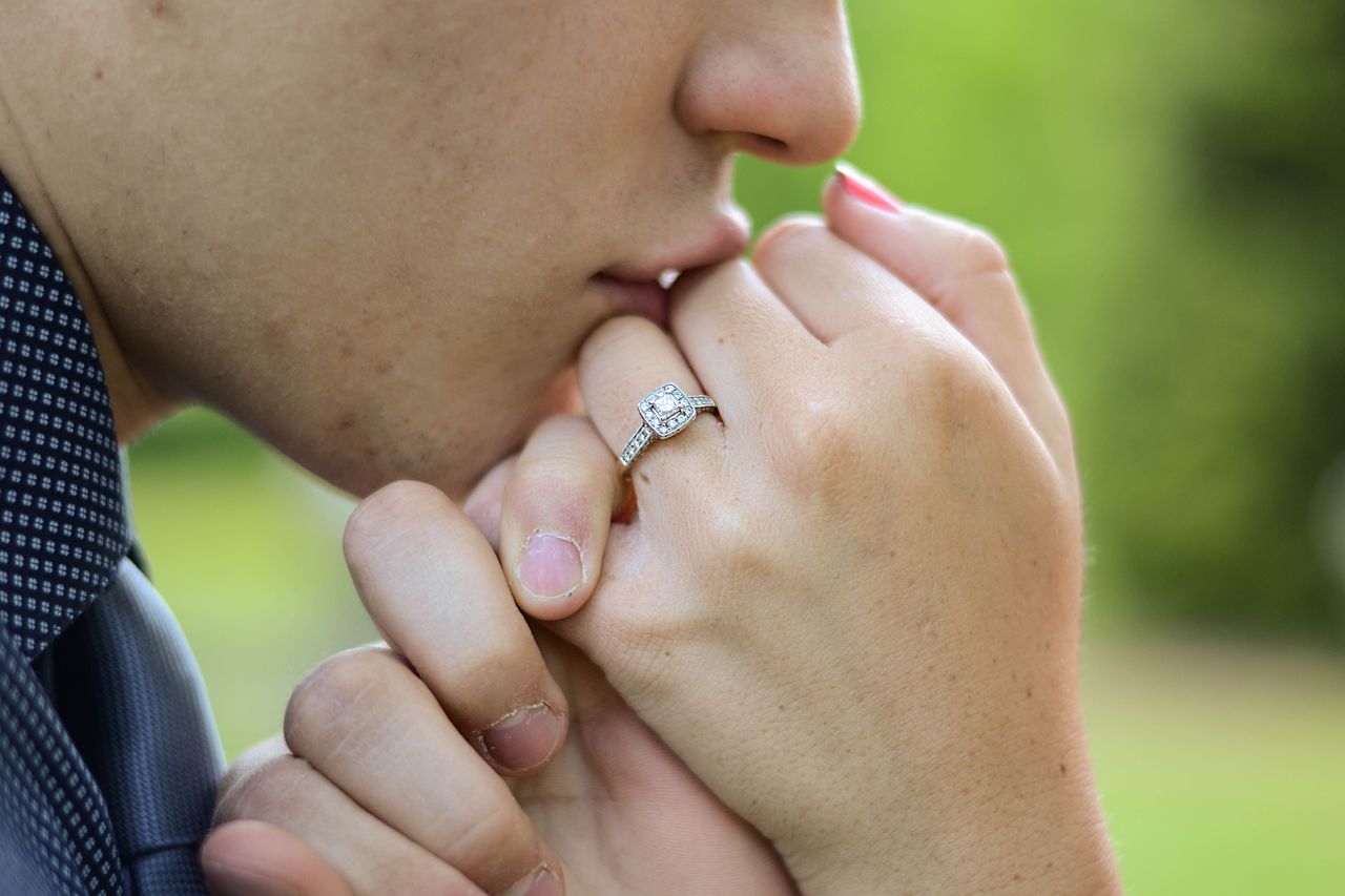 A man kisses the hand of his fiancee, wearing a halo engagement ring