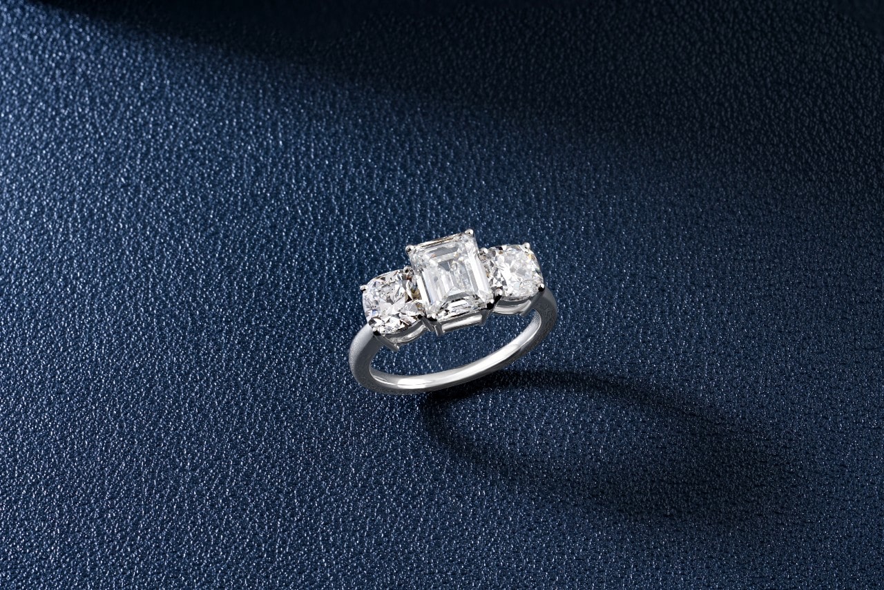 a white gold three stone engagement ring featuring an emerald cut center stone
