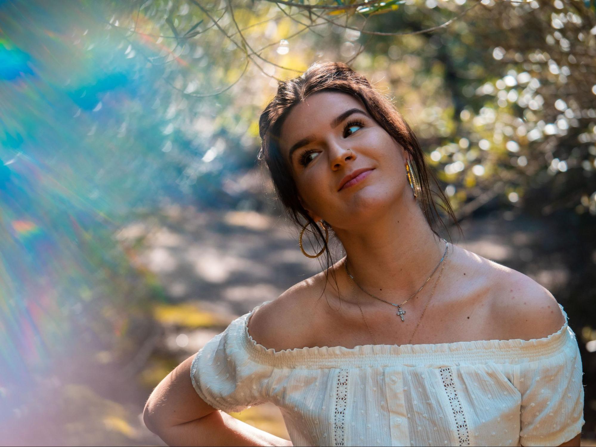 A woman strolls through a hiking path wearing a cross necklace and hoop earrings.