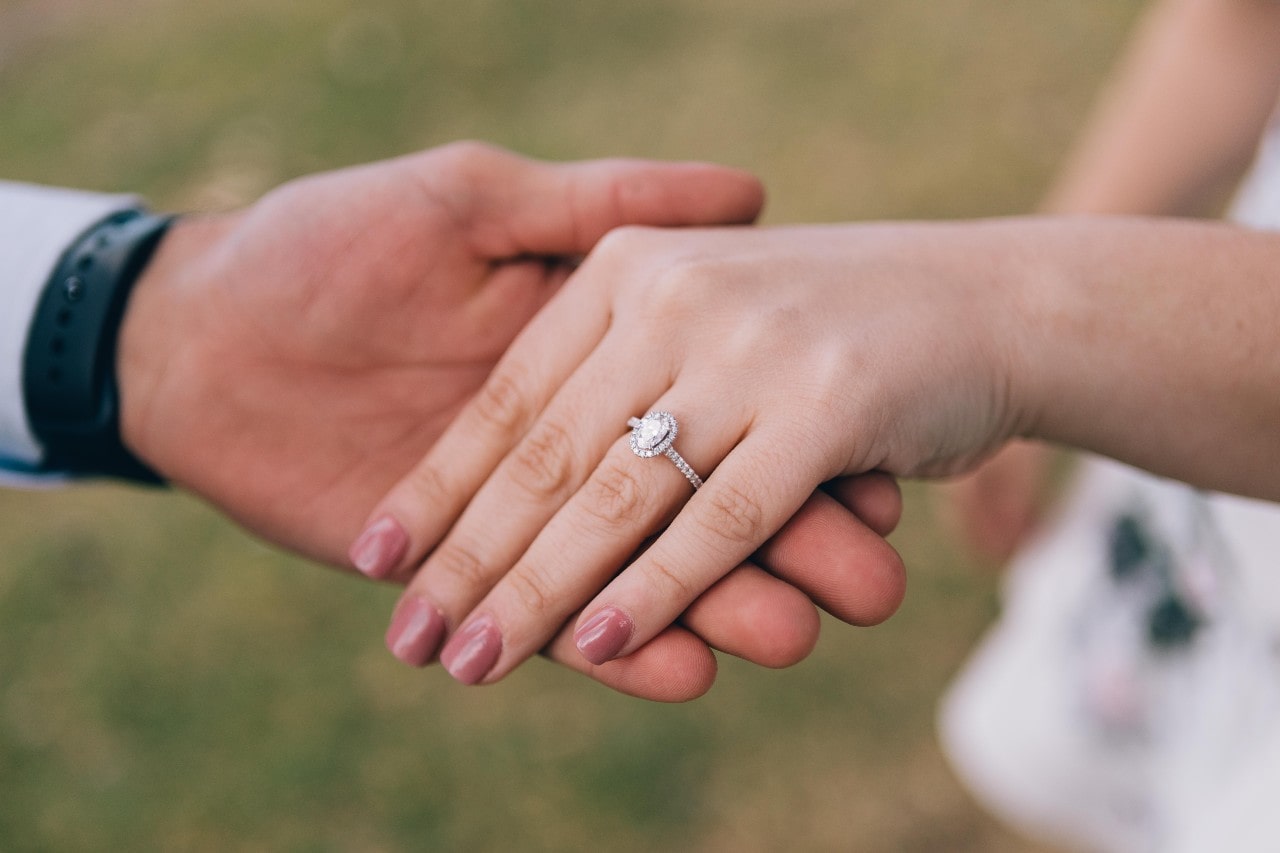 A man holding his bride’s hand, who is wearing an oval cut halo engagement ring