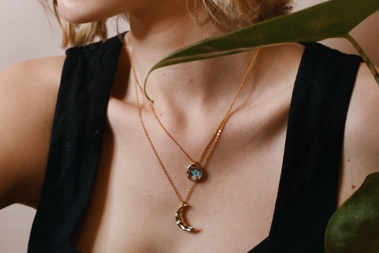 a woman wearing two gold pendant necklaces of varying lengths