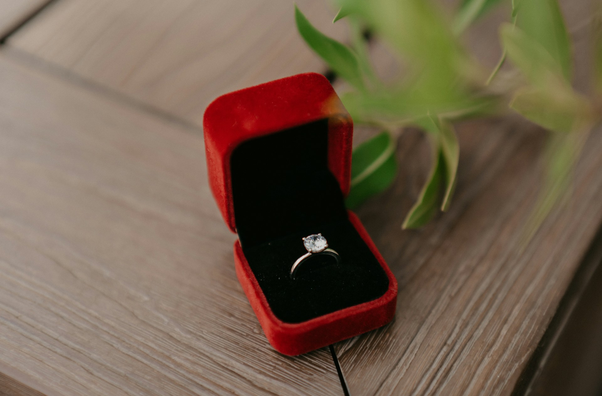 A classic diamond solitaire engagement ring displayed in a red velvet box on a wooden surface
