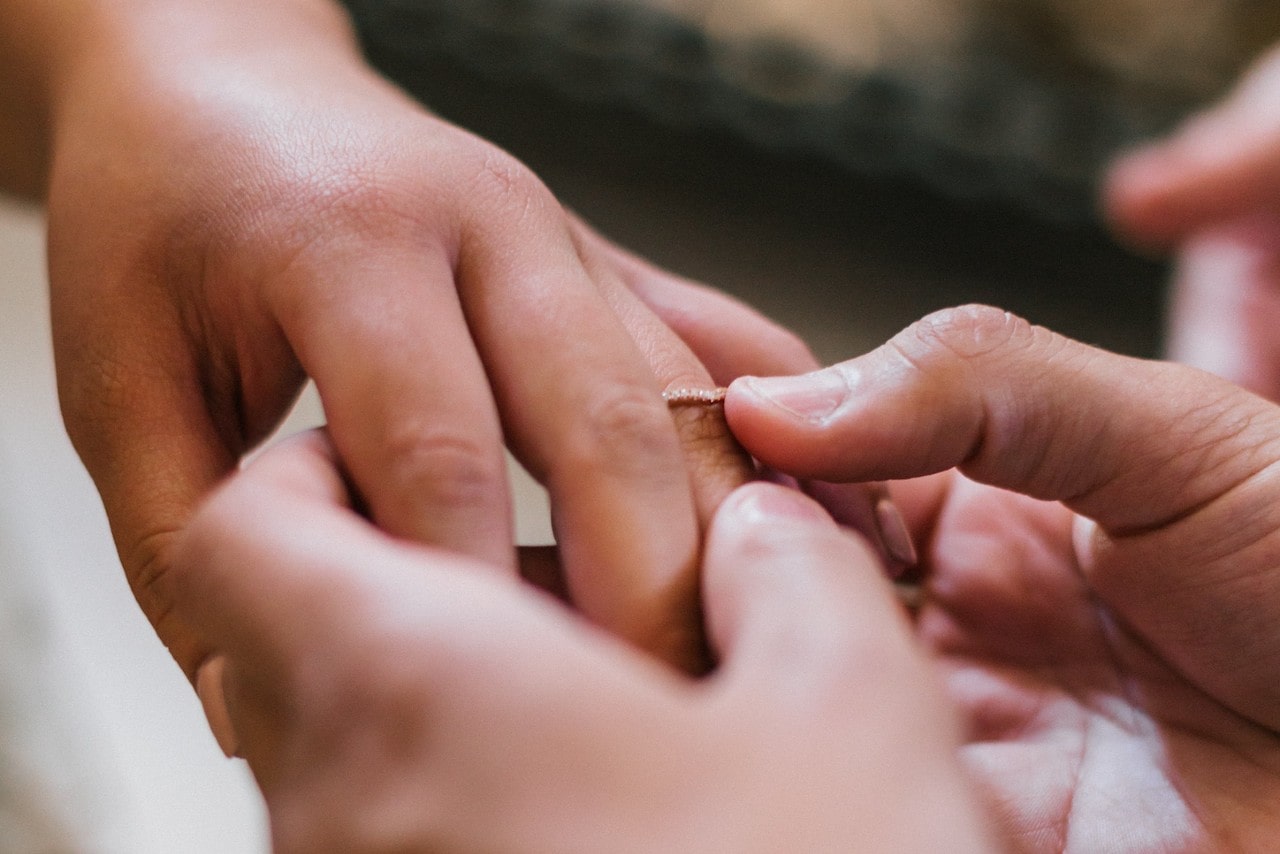 A close-up of a groom slipping a small but elegant eternity wedding band on his bride’s finger.
