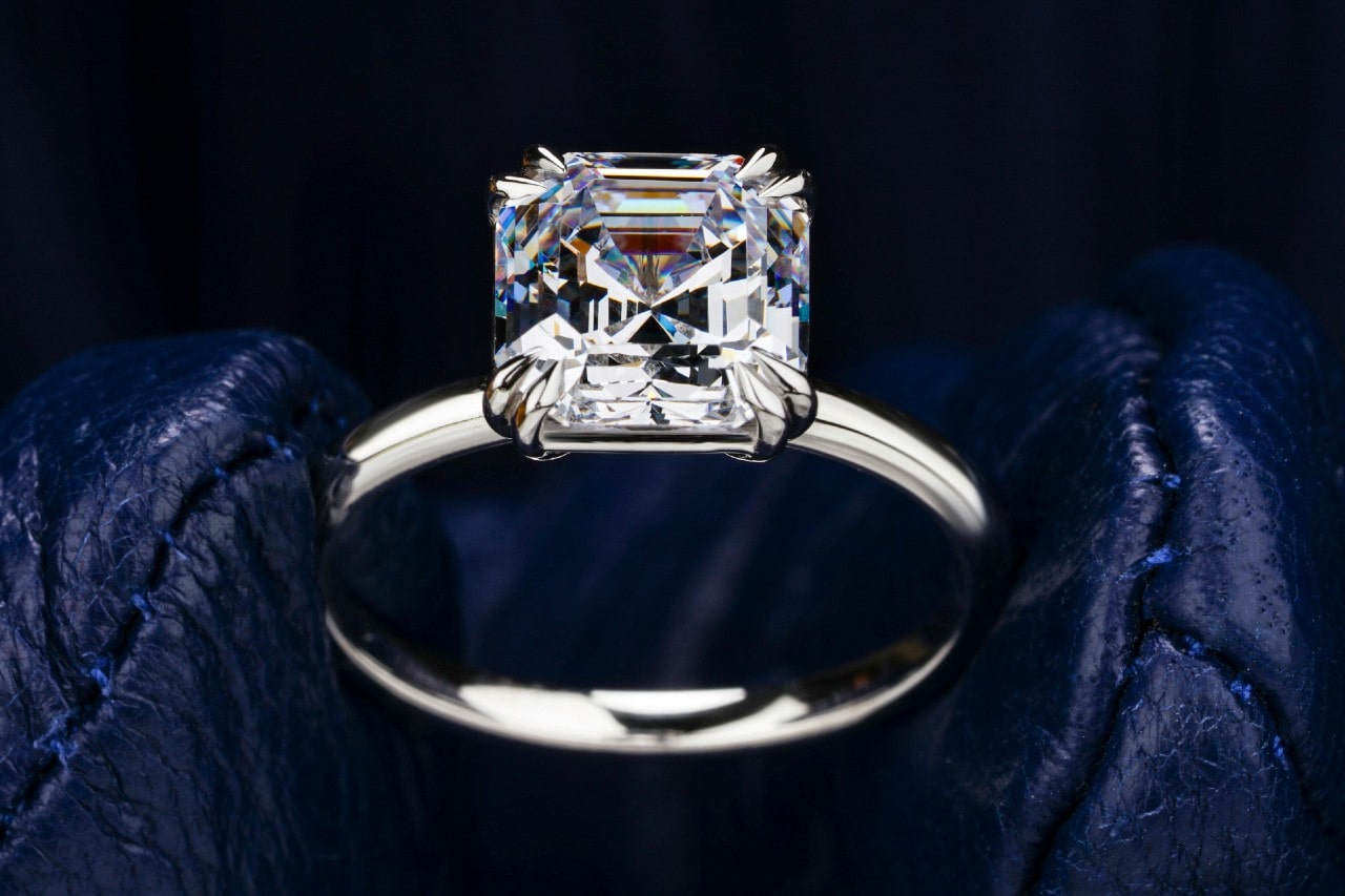 A solitaire diamond engagement ring set in white gold, posed on dark blue leather.