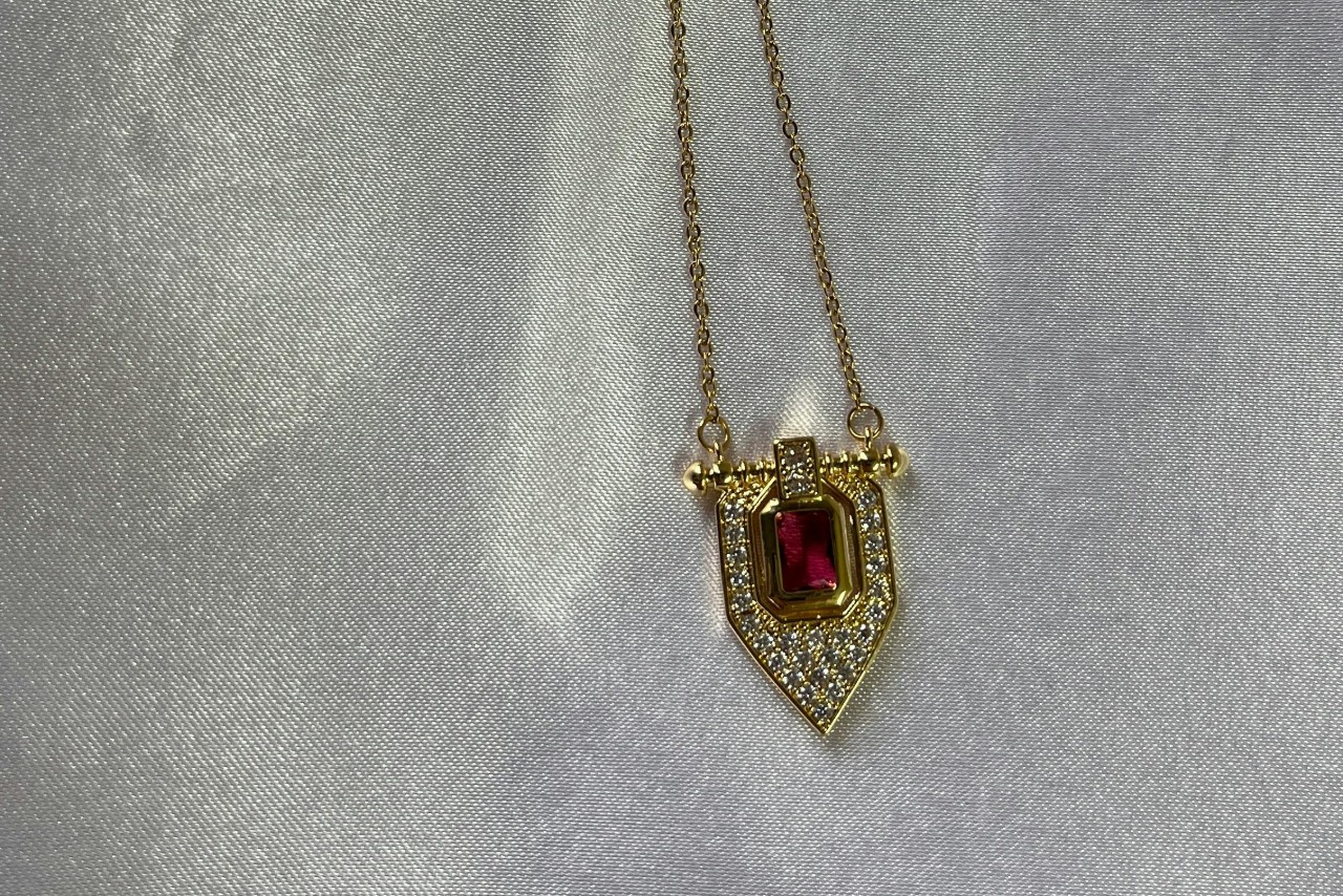 A yellow gold pendant necklace with a ruby center stone and diamond accents.