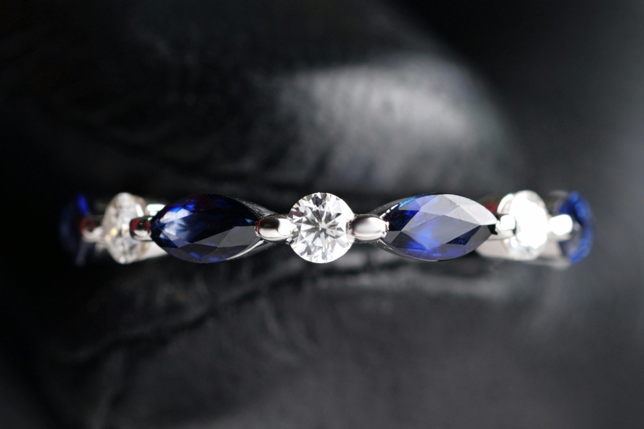 A close-up of a delicate prong wedding band featuring round cut diamonds and marquise cut sapphires.