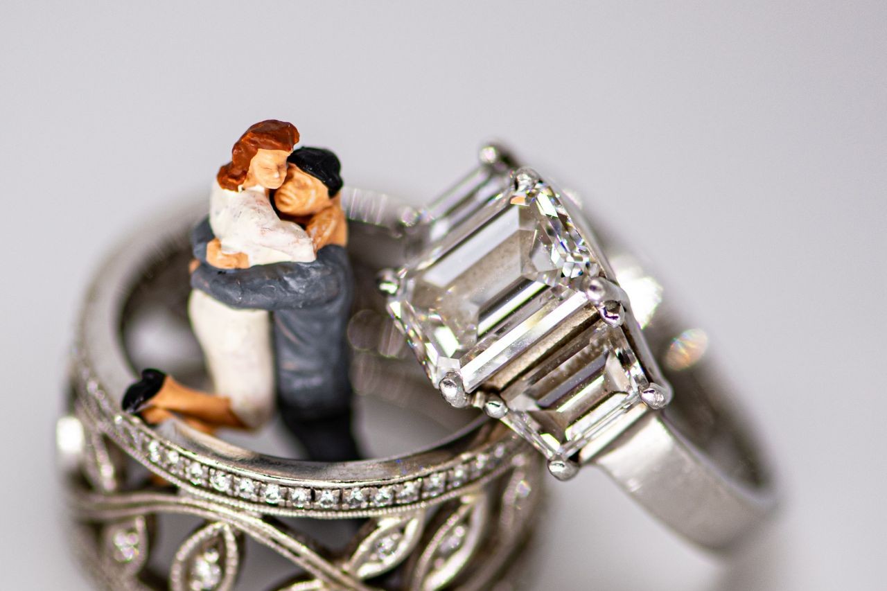 two white gold rings, one a three stone engagement ring, beside a wedding cake topper