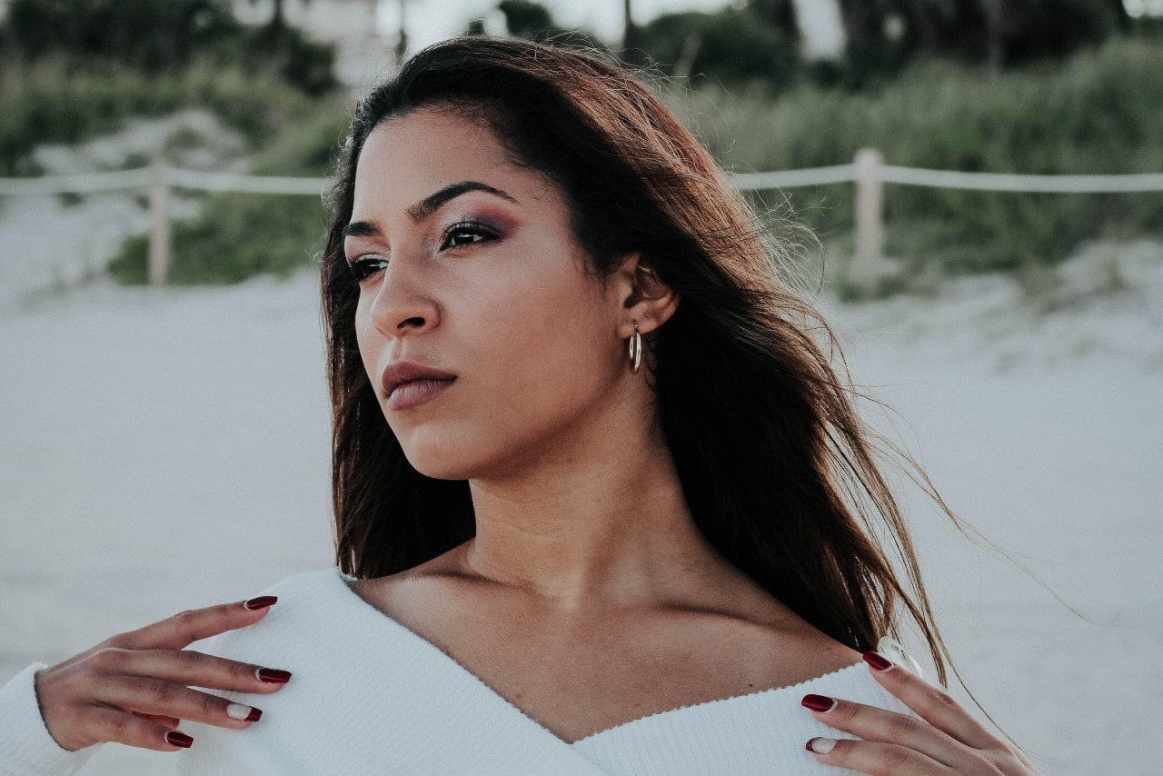 a woman on the beach looking away from the camera and wearing silver hoop earrings