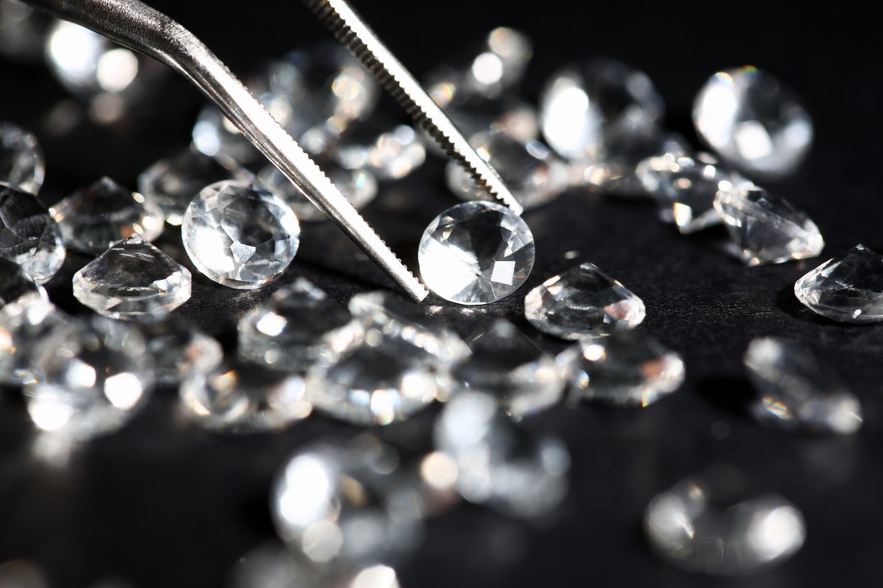 a jeweler selects a diamond with jewelry tweezers among a group of diamonds.