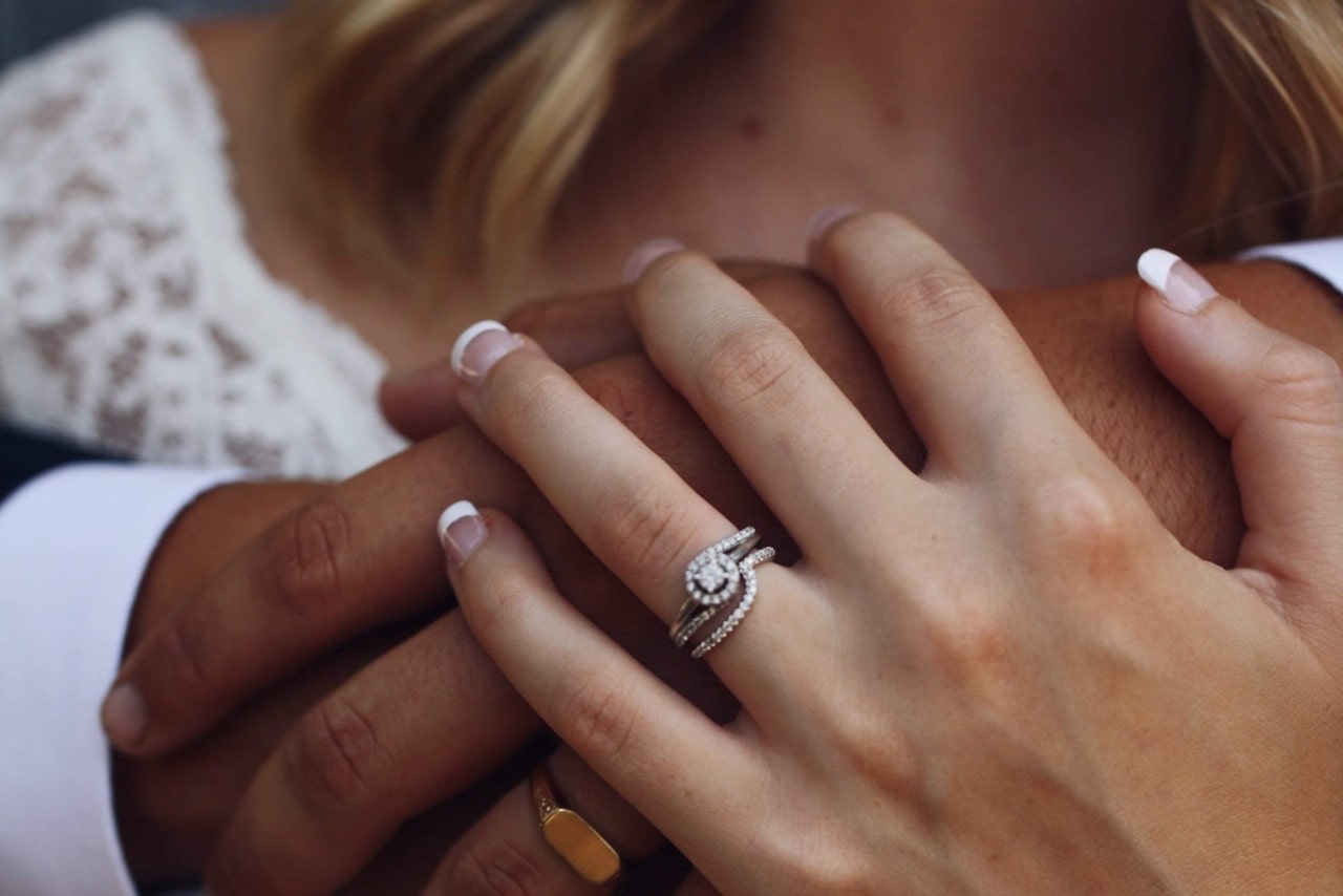 A woman wearing a contemporary round cut diamond ring embraces her husband