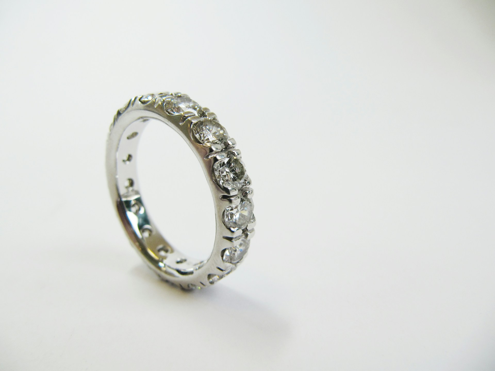 A close-up of a simple yet elegant eternity wedding band displayed on its side on a white backdrop.