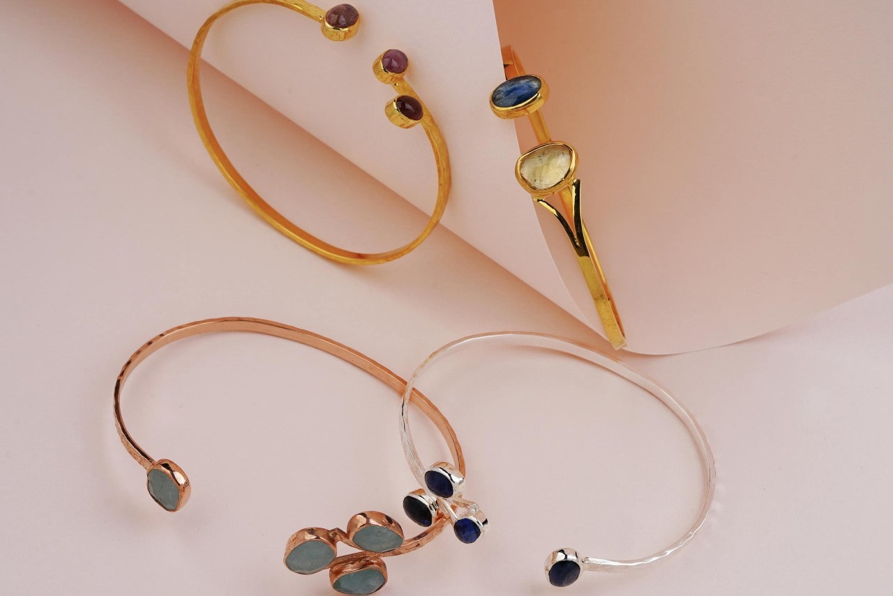 A close-up of four cuff bracelets of different metals with different gemstones.