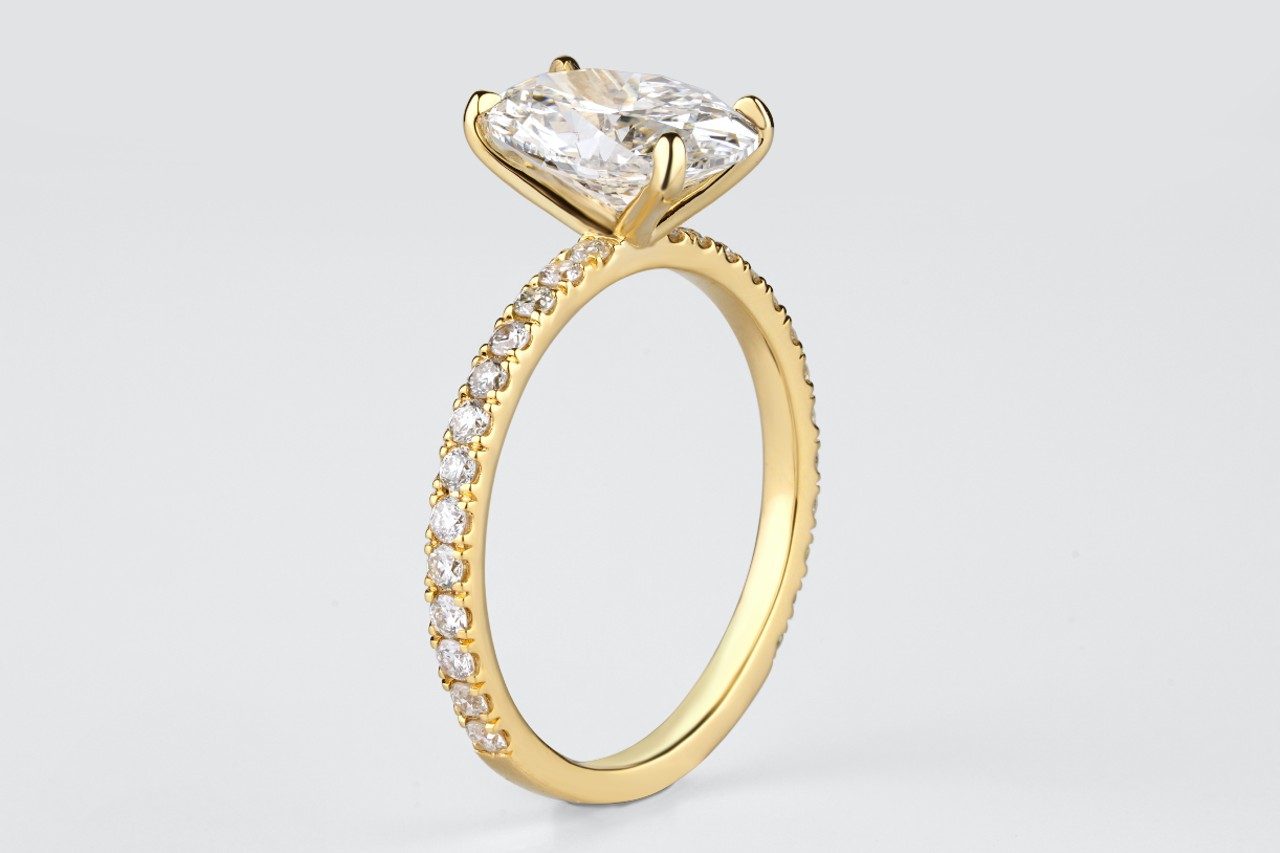 A close-up of a side stone engagement ring with a round center stone in a yellow gold prong setting.