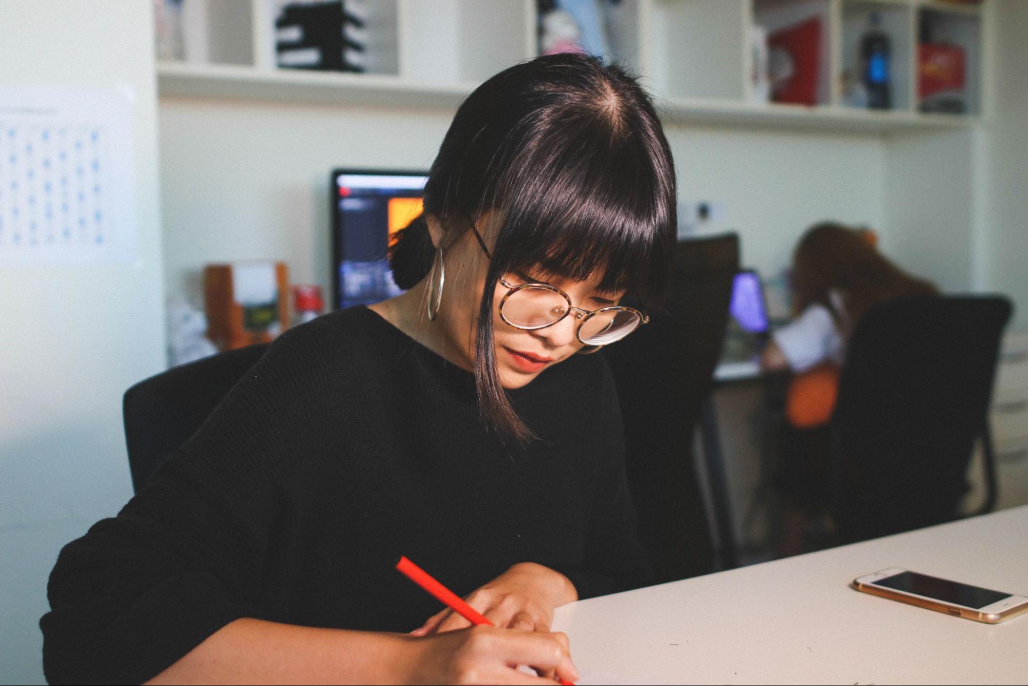 A woman writing with a red pen in an office and wearing hoop earrings