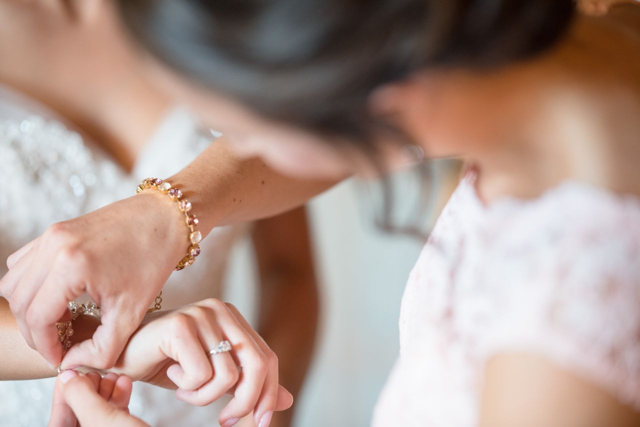 A woman putting a bracelet onto a bride's wrist, showcasing her beautiful gold diamond bracelet.