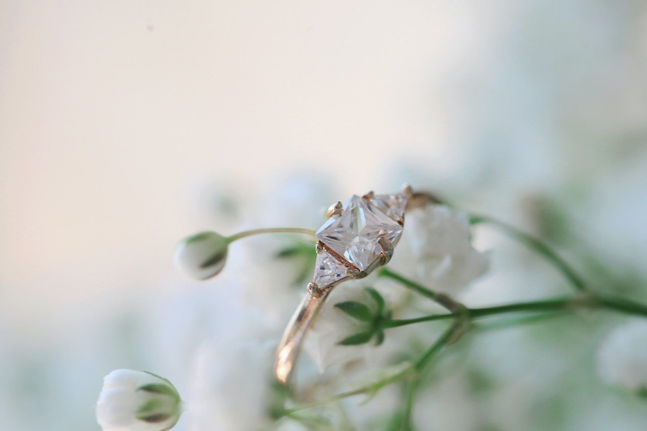 a yellow gold engagement ring featuring a princess cut center stone and two triangular shaped side stones