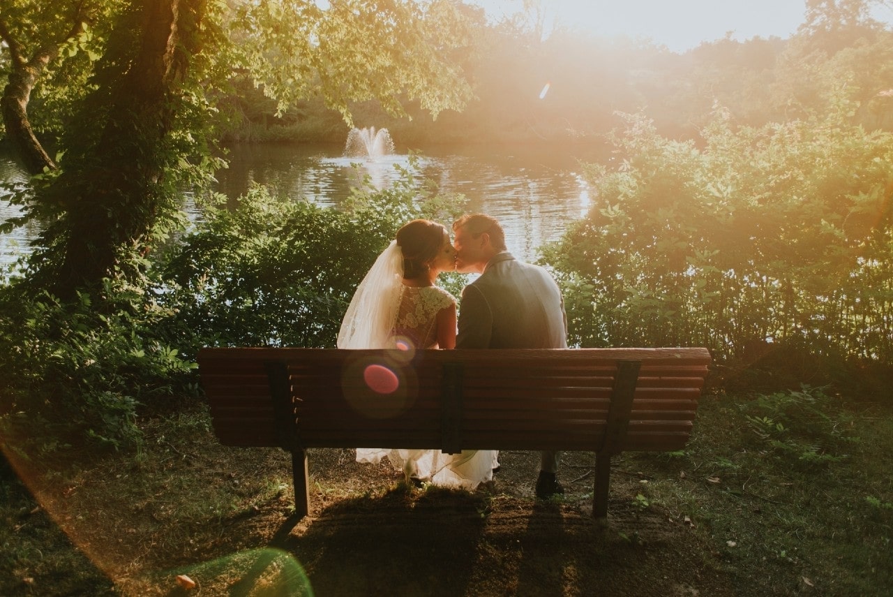 a bride and groom embracing on a bench in a park