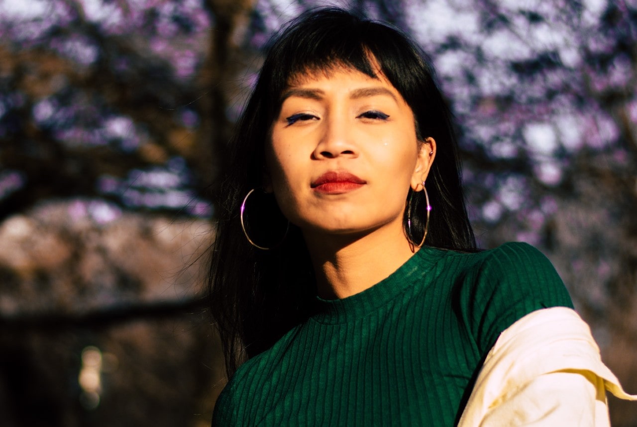 A woman in a green top looking into the camera and wearing hoop earrings