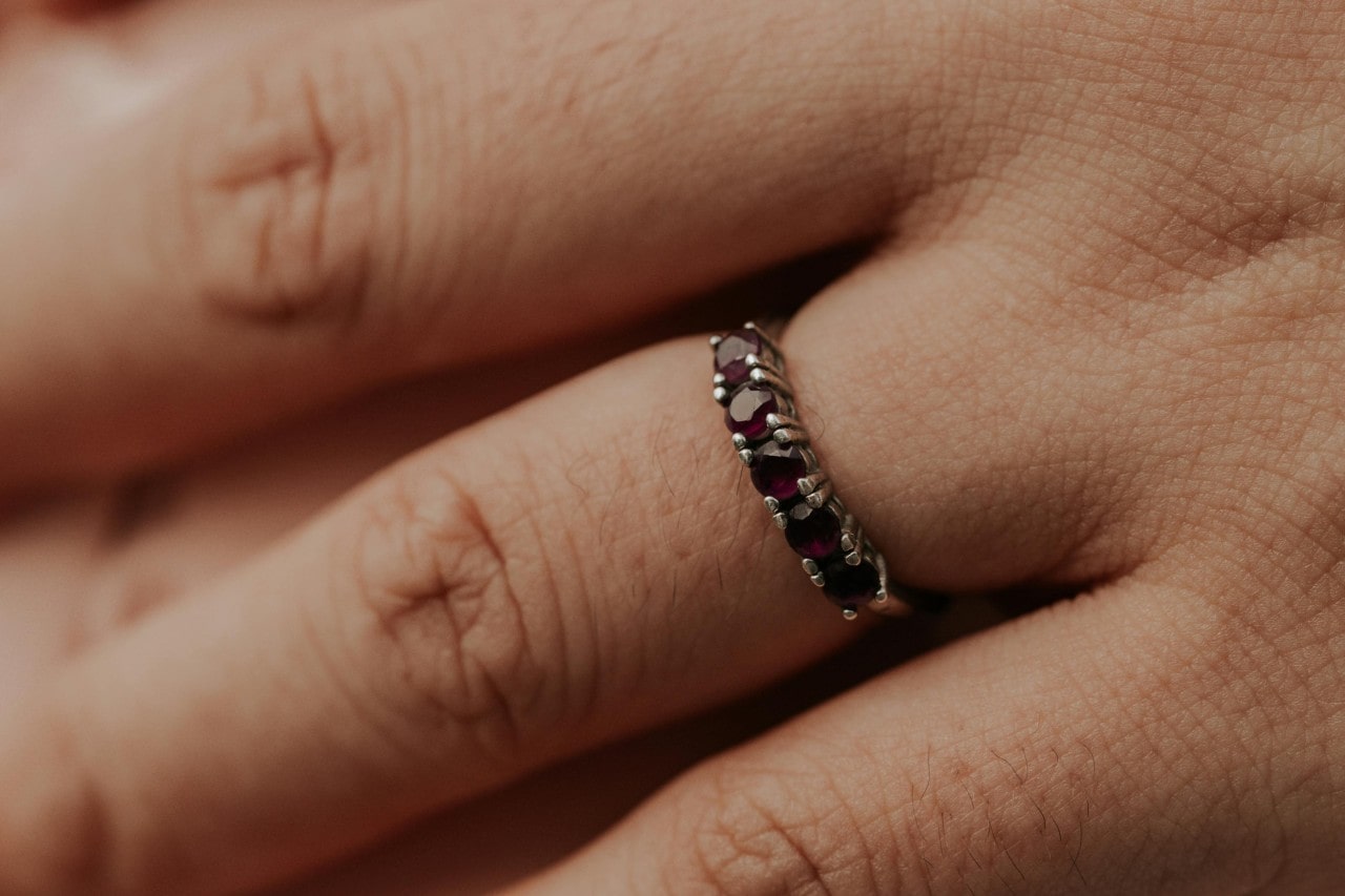 A close-up of a woman’s hand, a ruby prong wedding band on her finger.