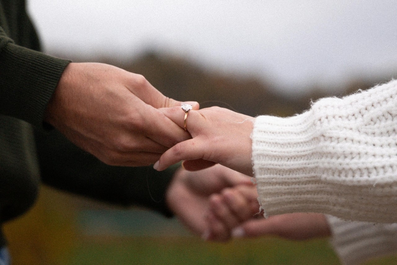 A close-up of a warmly dressed couple’s hands, with emphasis on her solitaire ring.