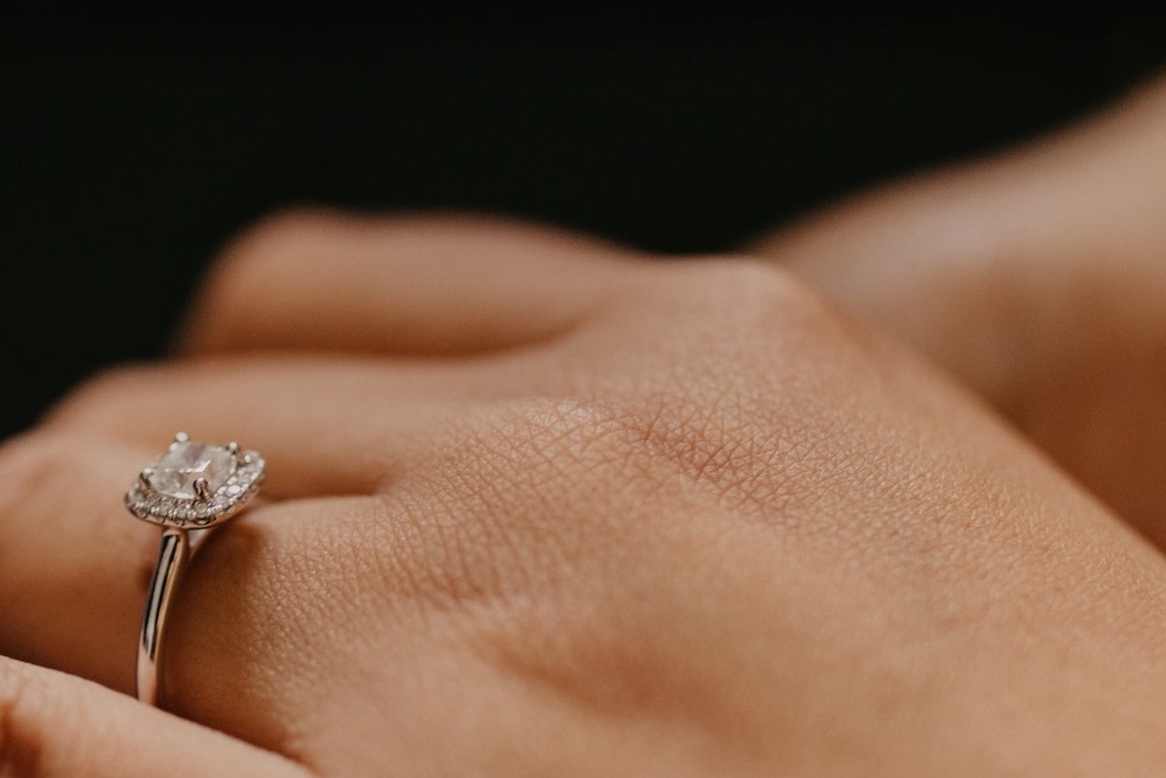 A close-up of a halo princess-cut diamond engagement ring on a woman’s hand