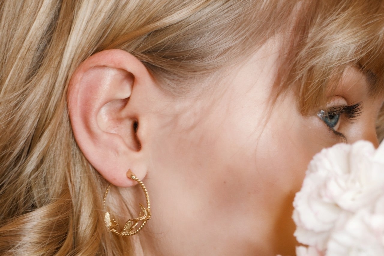 close up image of a woman looking away from the camera, wearing a sculptural gold hoop