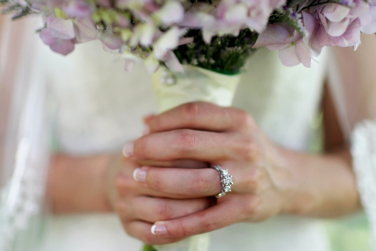 a bride holding her bouquet and wearing a white gold three stone engagement ring