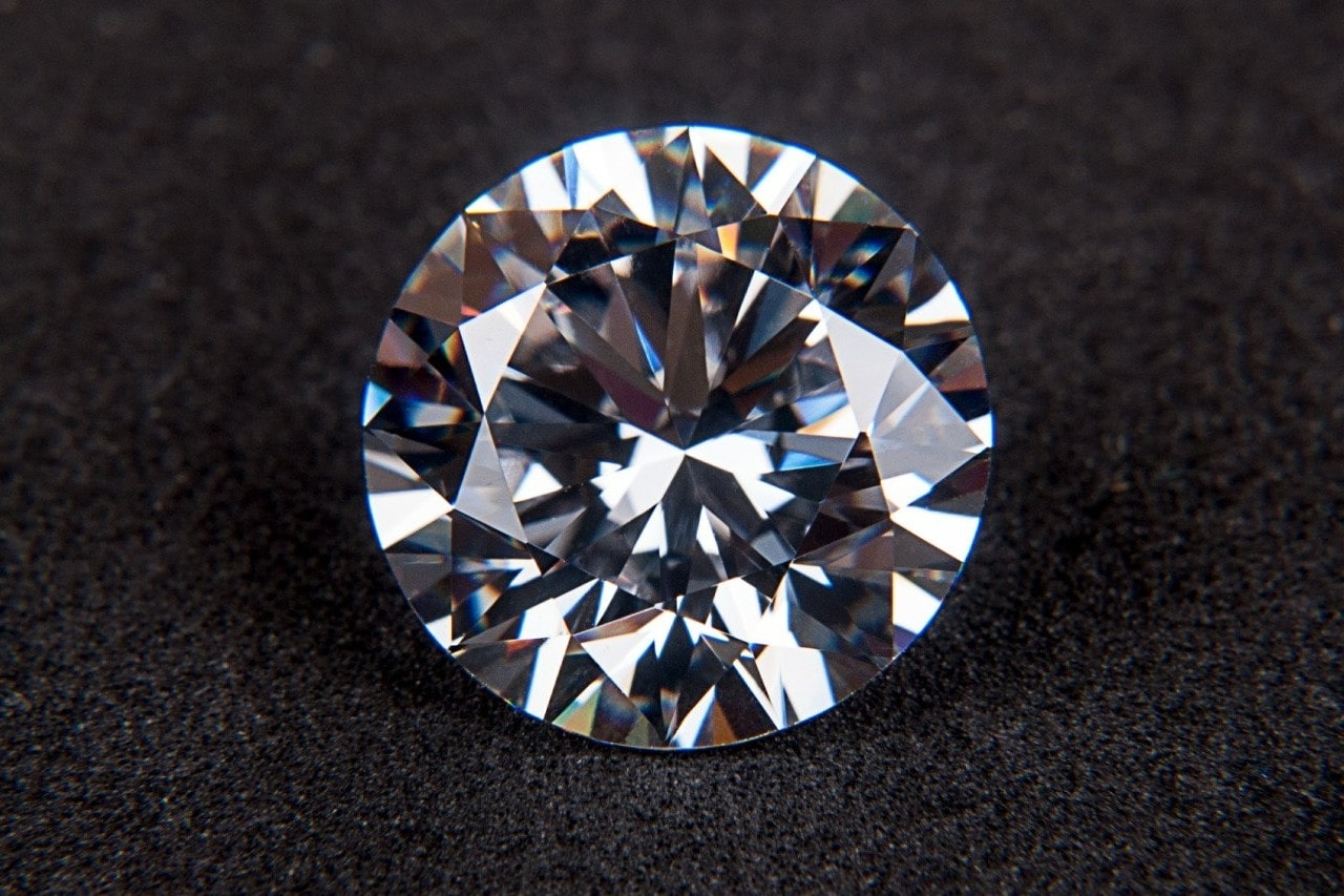 A round-cut diamond sits on a black surface.