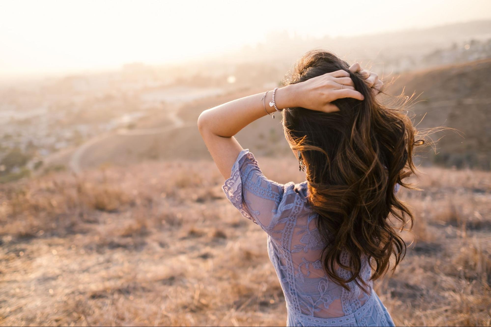 a lady wearing fashion bracelets, standing outside with a city in the distance