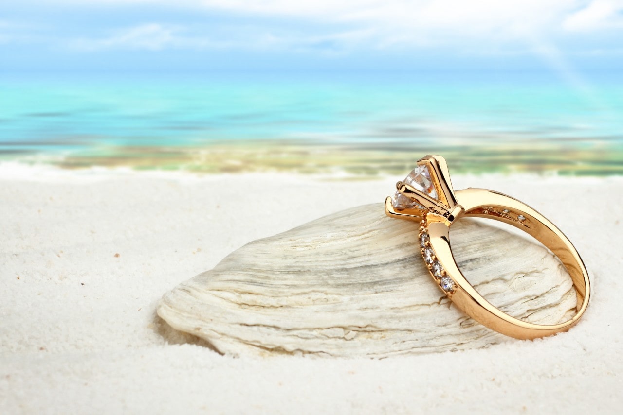 A yellow gold diamond ring on a beach