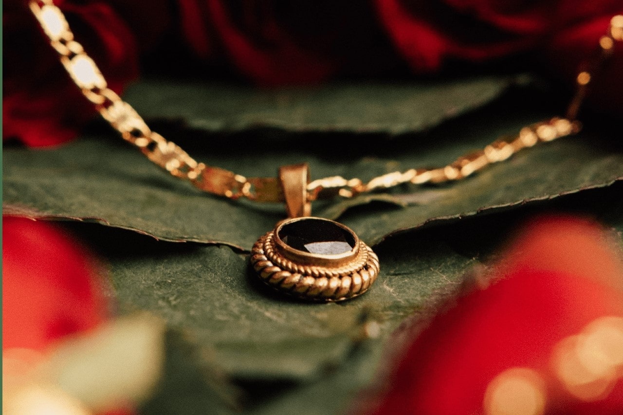 Gold necklace with a black gemstone sitting on a leaf