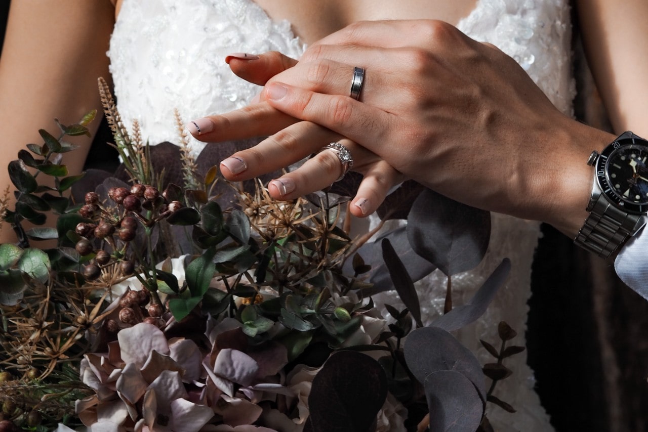 a bride and groom showing off their rings, the bride holding a fall bouquet