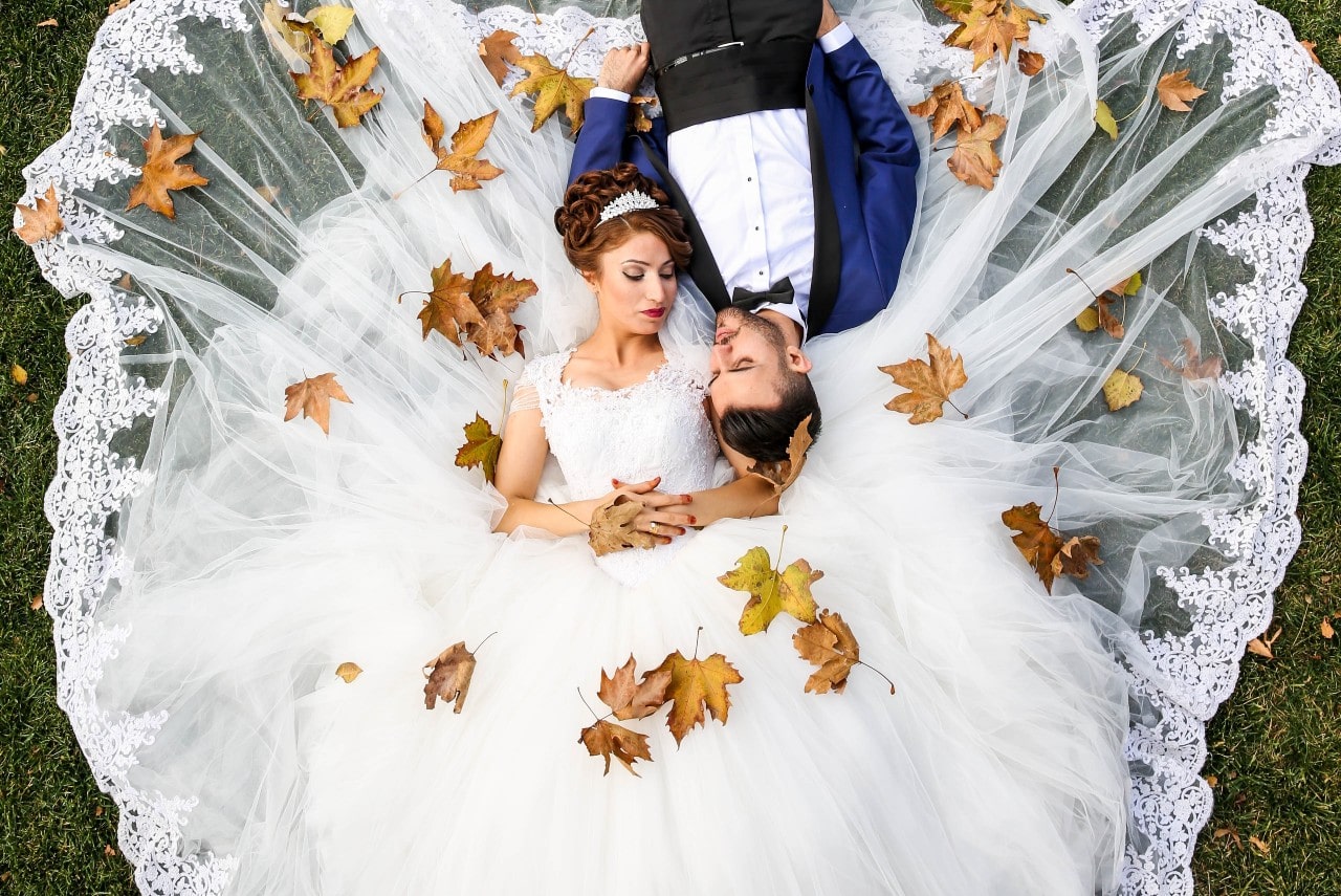 a bride and groom lying in the grass, covered in fall leaves