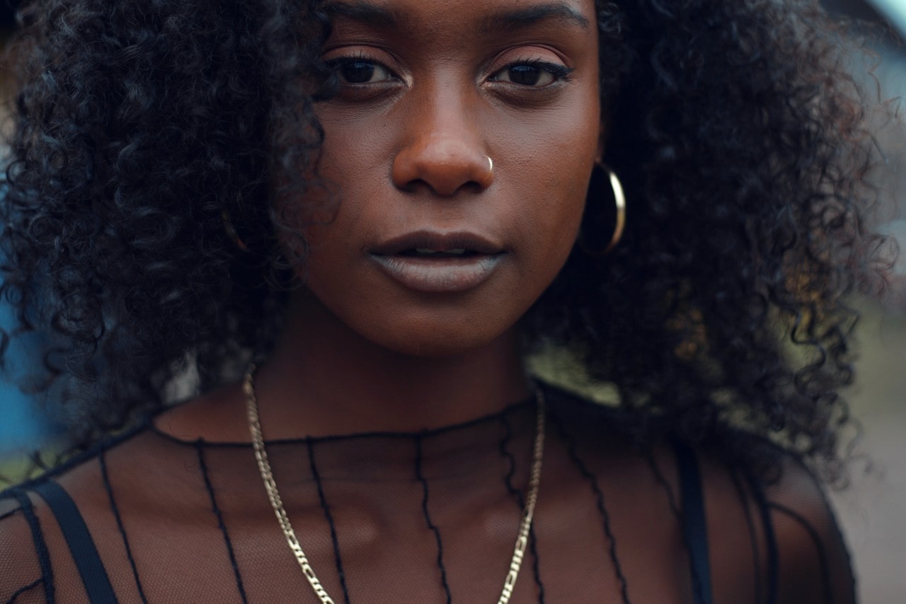 a woman wearing a black mesh top with gold hoop earrings and a figaro chain necklace.