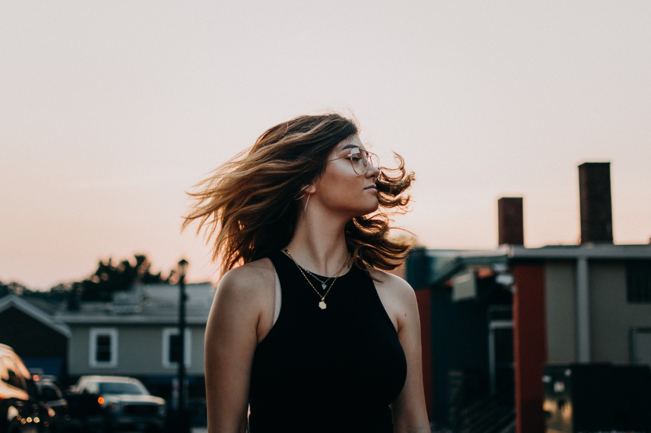 A woman shakes her head, wearing two layered necklaces, while the sunsets.