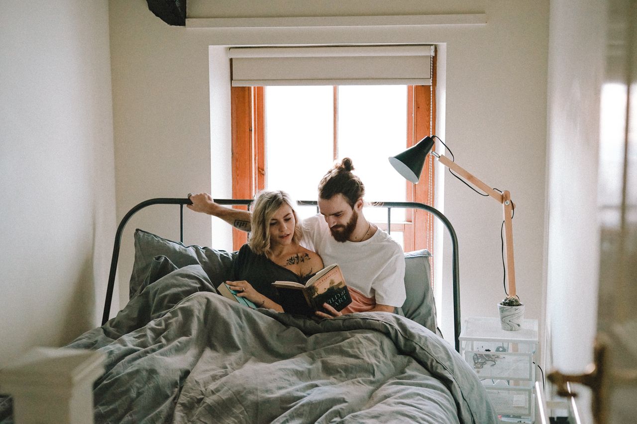 A couple in bed discuss the man’s book while the woman opens her own.