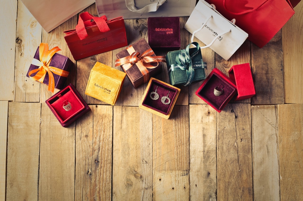 An array of jewelry gifts, some wrapped, some opened, sits on a hardwood floor.