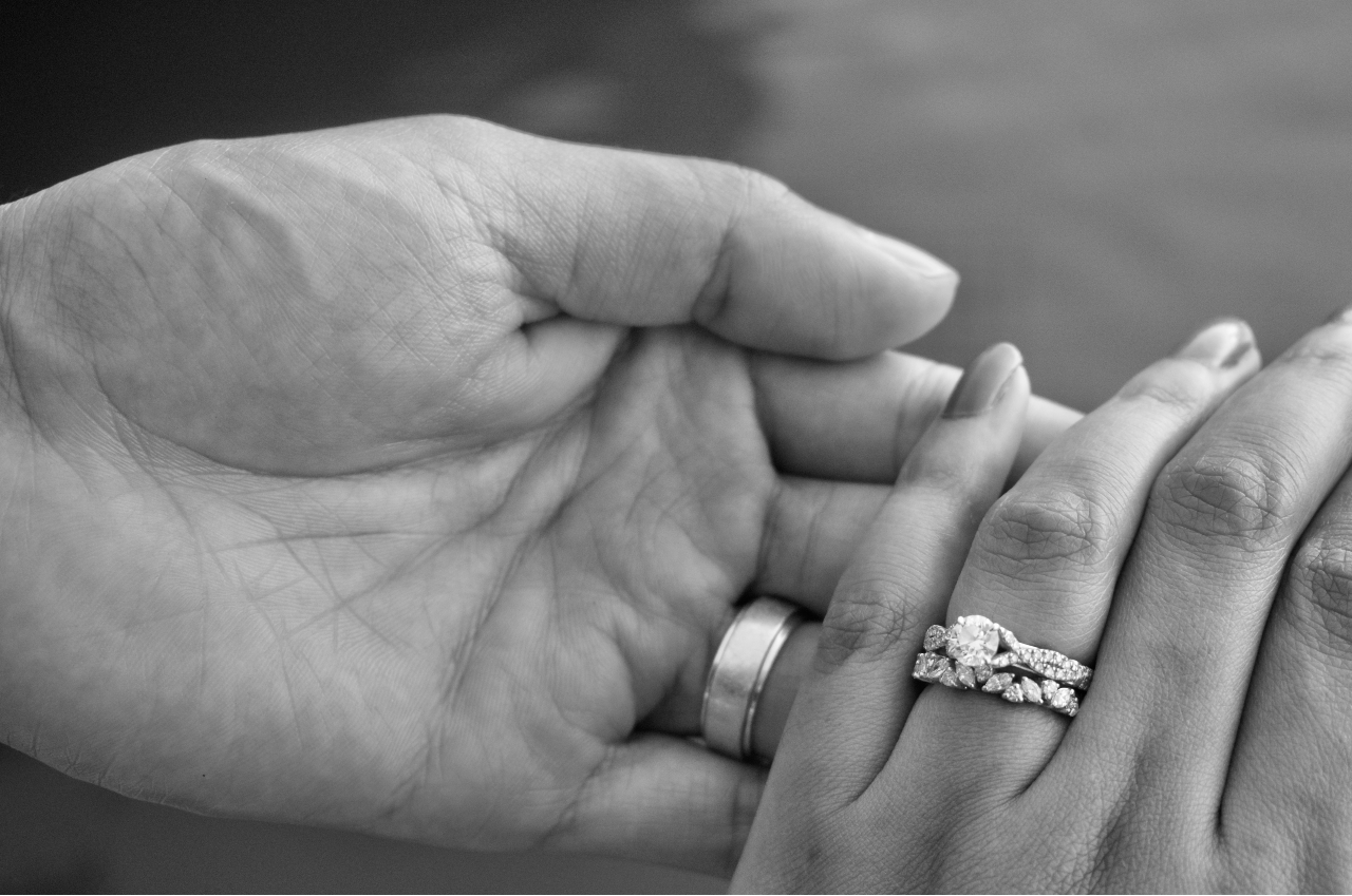 two hands clasped together wearing bridal rings