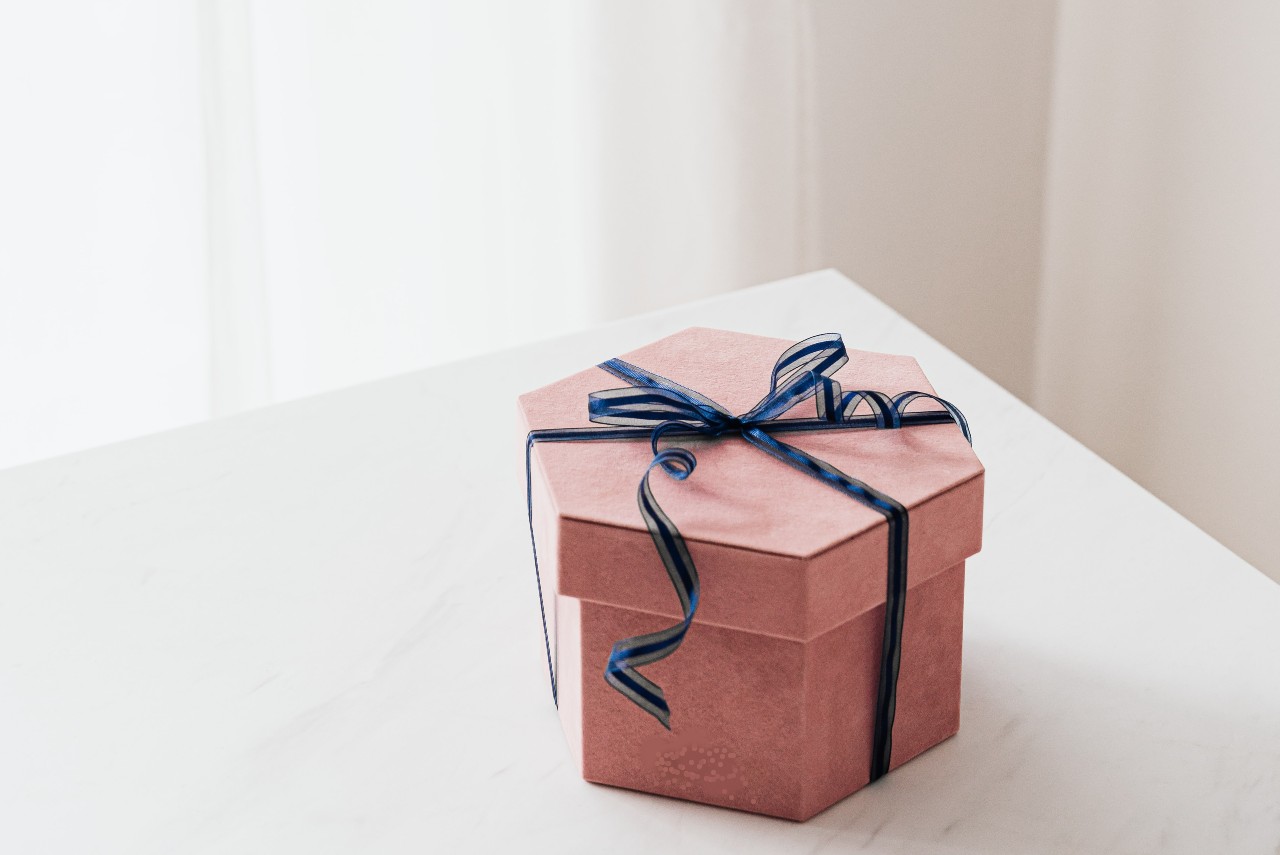A pink hexagon-shaped gift box with a blue ribbon sits on a table.