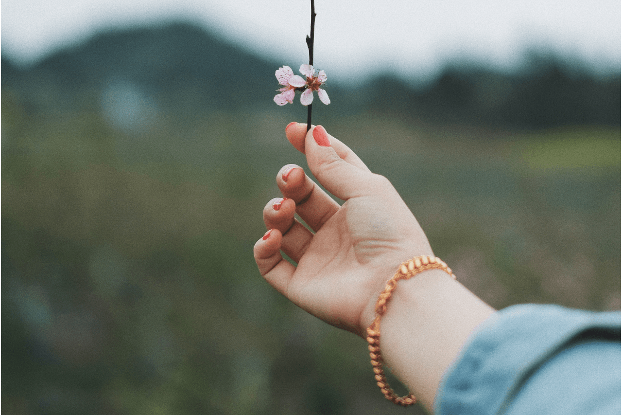 a woman’s arm holding up a flower and wearing a rose gold bracelet