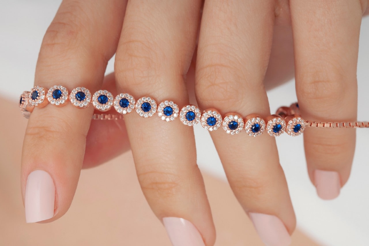 a woman’s hand holding a rose gold line bracelet featuring sapphires and diamonds
