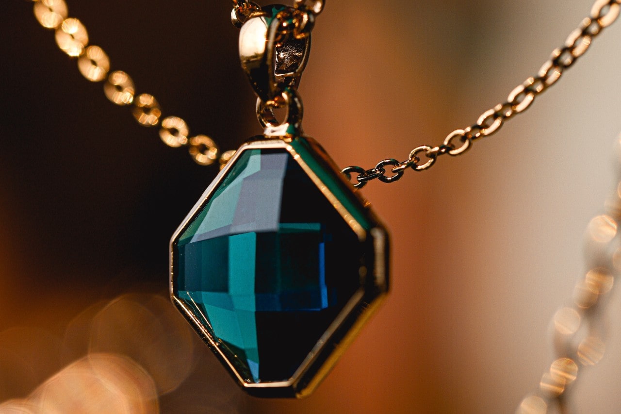 close up image of a gold pendant necklace with a blue green gemstone