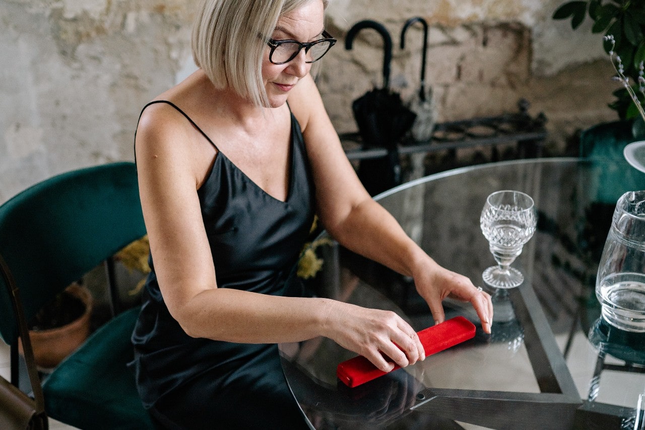 A woman opening a long, thin red jewelry box at a glass table